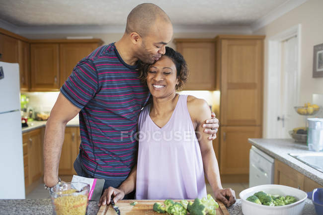 Любящий муж обнимает жену и готовит на кухне — стоковое фото