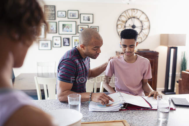 Father helping teenage son with homework in kitchen — Stock Photo