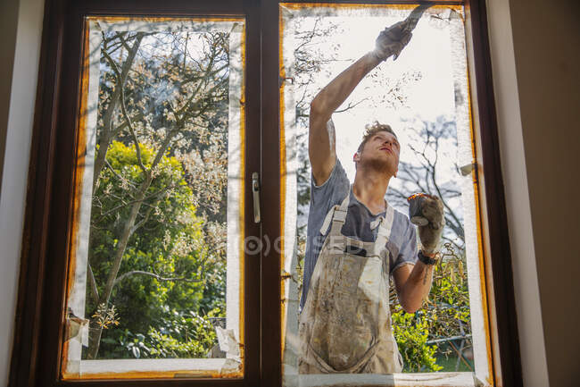 Художник-мужчина расписывает наружное окно дома — стоковое фото