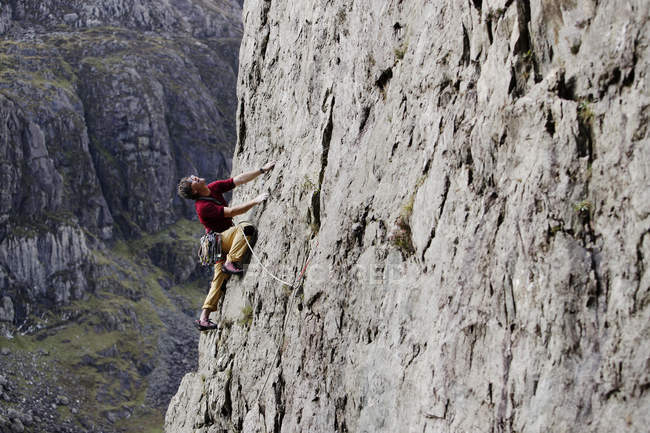 Hombre escalador escalando roca cara, mirando hacia arriba - foto de stock