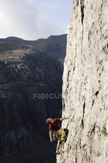 Hombre escalador escalando gran cara de roca, mirando hacia arriba - foto de stock
