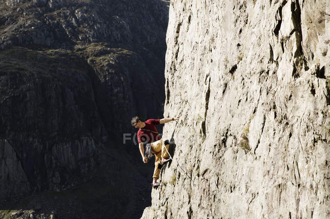 Masculino escalador de rocha escalar grande rosto de rocha, olhando para baixo sobre o ombro — Fotografia de Stock