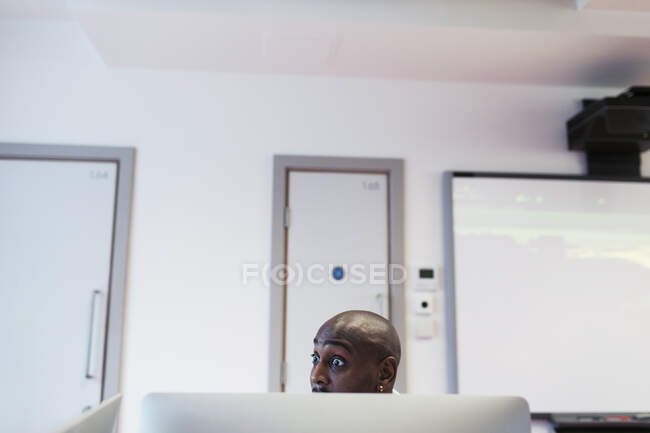 Sorprendido estudiante universitario comunitario masculino usando computadora en el aula - foto de stock