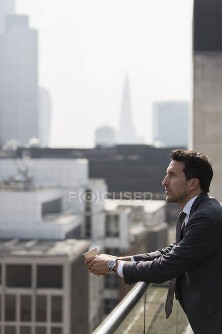 Homme d'affaires réfléchi sur un balcon ensoleillé et urbain — Photo de stock