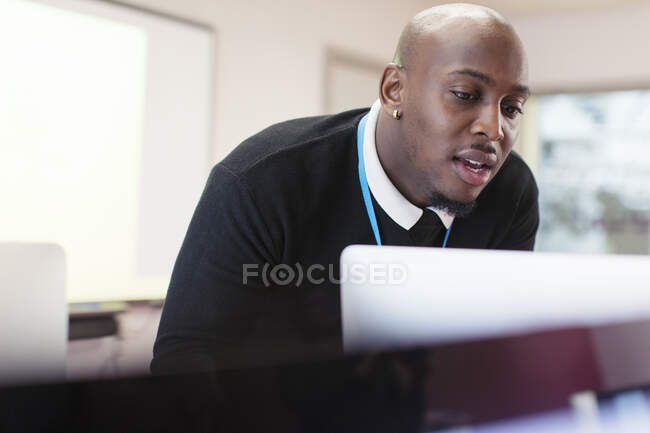 Instructor masculino enfocado en la computadora en el aula - foto de stock