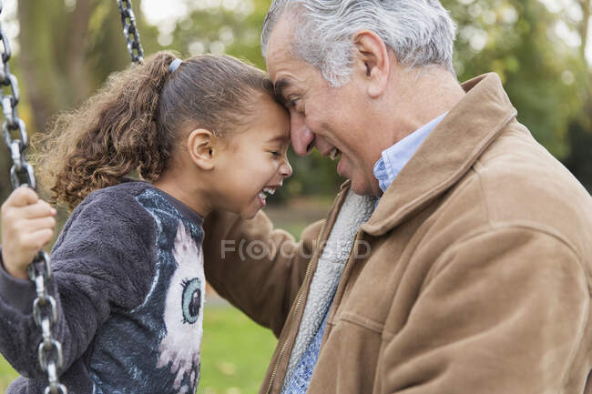 Playful affectionate grandfather and granddaughter on swing at playground — Stock Photo
