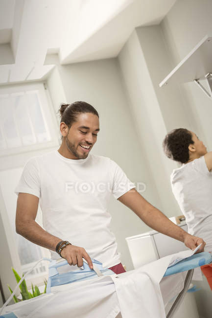 Young man doing laundry, ironing shirt in laundry room — Stock Photo