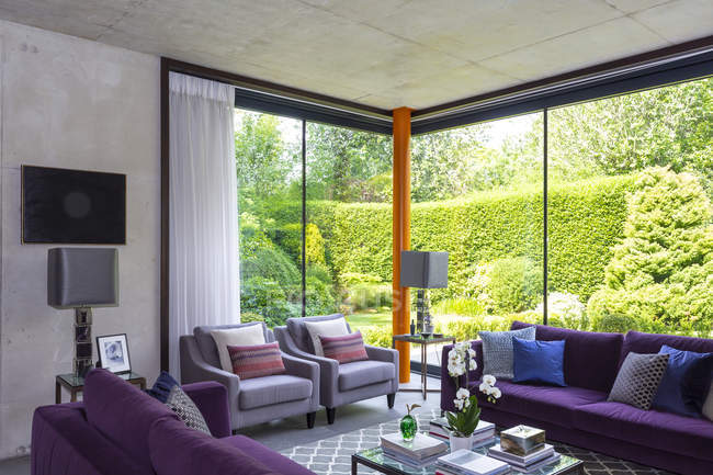 Sala de estar moderna com mobiliário roxo e vista para o jardim ensolarado — Fotografia de Stock