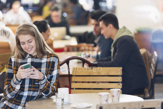 Sorrindo jovem mulher usando telefone inteligente no café — Fotografia de Stock
