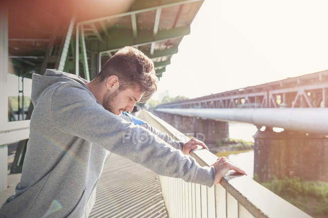 Male runner stretching, leaning against sunny urban railing — Stock Photo