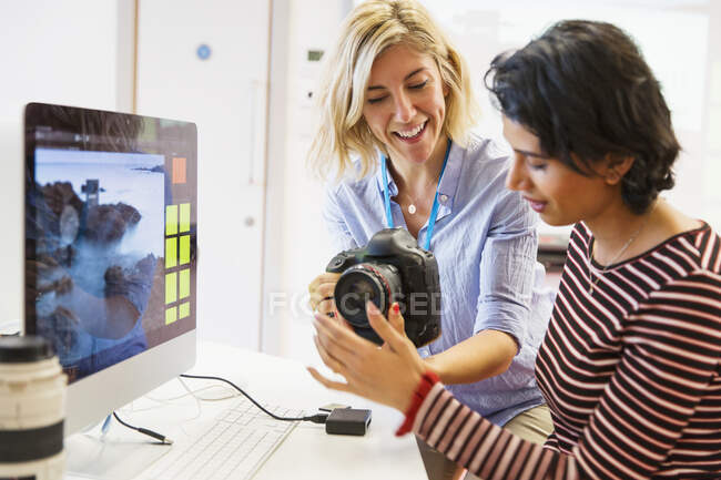 Female photography instructor helping student with digital camera at computer in classroom — Stock Photo