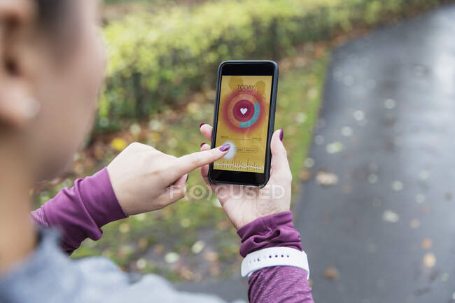 Жіночий бігун перевіряє частоту серцевих скорочень на смартфоні на шляху — стокове фото