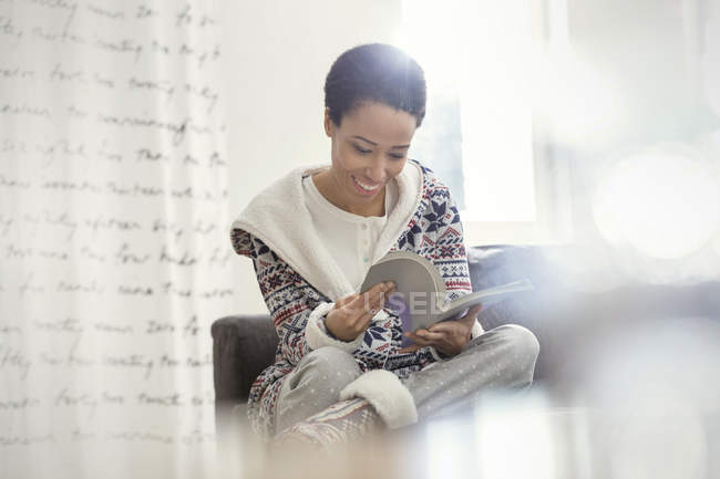 Улыбающаяся женщина в пижаме читает книгу — стоковое фото