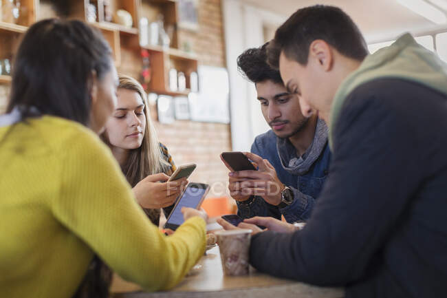 Amigos adultos jóvenes usando teléfonos inteligentes en la mesa de la cafetería - foto de stock