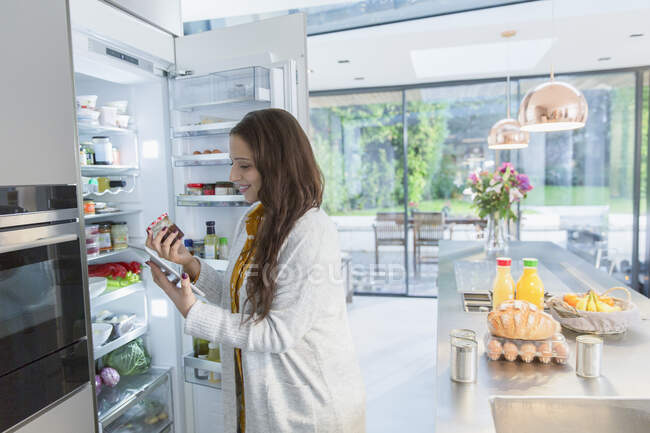Mulher com tablet digital na geladeira na cozinha — Fotografia de Stock