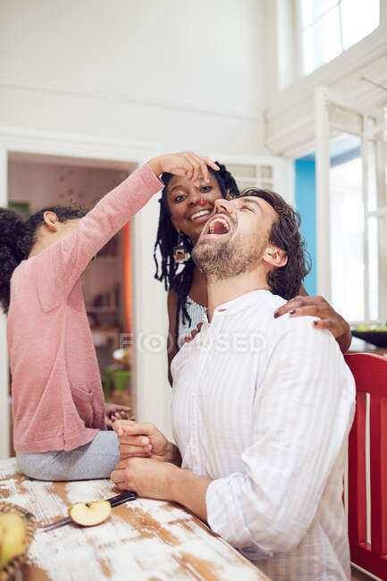Verspielte Tochter füttert Vater am Küchentisch — Stockfoto
