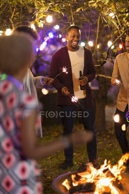 Friends with sparklers drinking beers around fire pit — Stock Photo