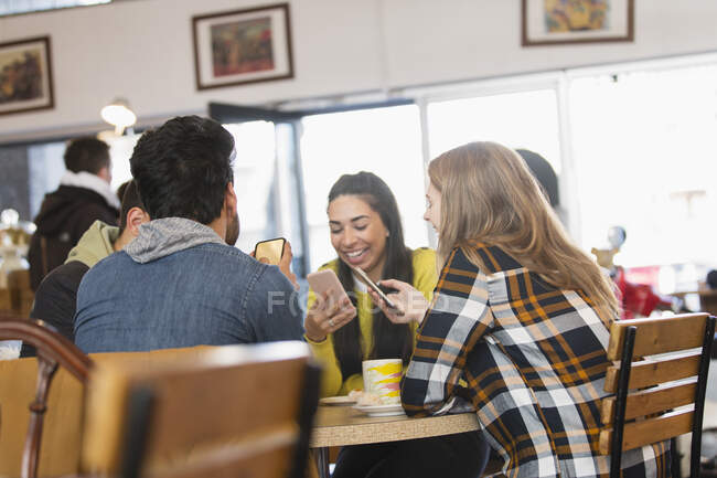 Young adult friends using smart phones in cafe — Stock Photo
