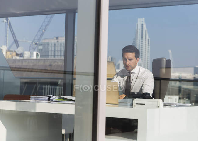 Empresario enfocado que trabaja en oficina soleada, moderna, urbana - foto de stock