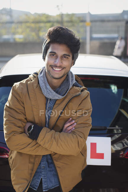 Portrait confident young man with learners permit leaning against car — Stock Photo