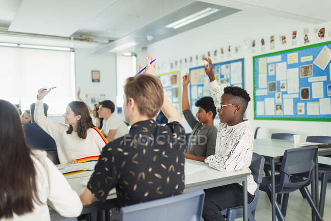 High school students with hands raised asking questions during lesson in classroom — Stock Photo