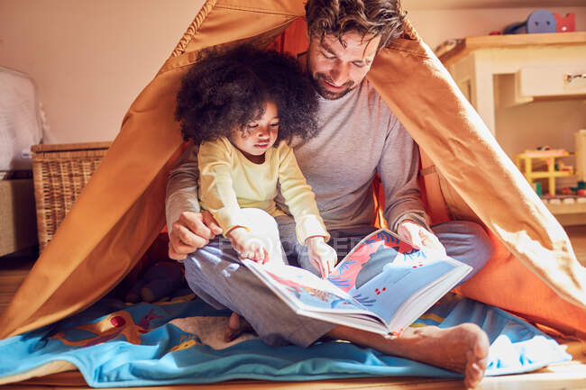 Father and daughter reading book in teepee — Stock Photo