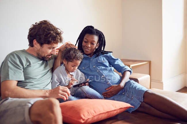 Giovane famiglia incinta utilizzando smart phone sul divano del soggiorno — Foto stock