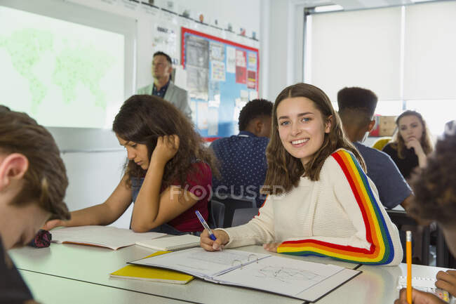 Portrait confiant lycéenne prenant des notes pendant les cours de géographie en classe — Photo de stock