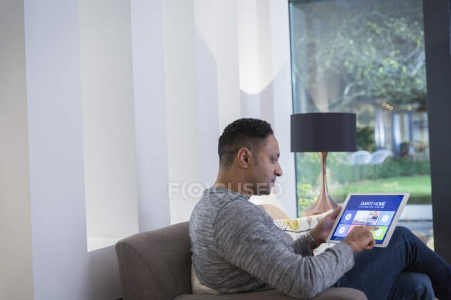 Système d'alarme maison intelligente de réglage de l'homme de tablette numérique sur le canapé du salon — Photo de stock