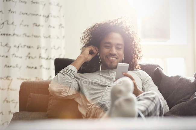 Giovane uomo rilassante, ascoltando musica con cuffie e lettore mp3 sul divano — Foto stock