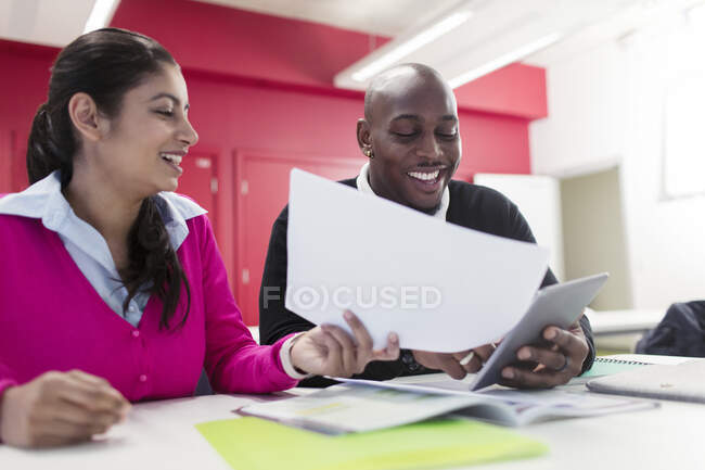 Lächelnde Gemeinschaftsschüler mit Papierkram und digitalem Tablet am Schreibtisch im Klassenzimmer — Stockfoto