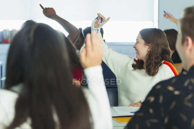 High school students with hands raised in classroom — Stock Photo