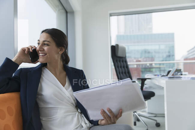Mujer de negocios sonriente hablando por teléfono inteligente en la oficina - foto de stock