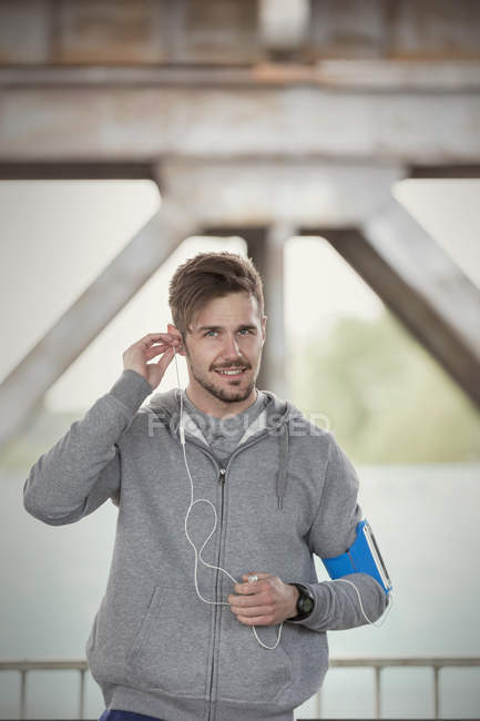 Portrait confident young male runner with earphones and mp3 player arm band — Stock Photo