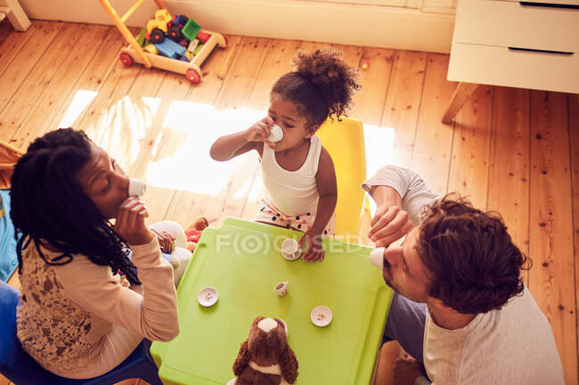 Familia joven disfrutando de una fiesta de té imaginaria - foto de stock