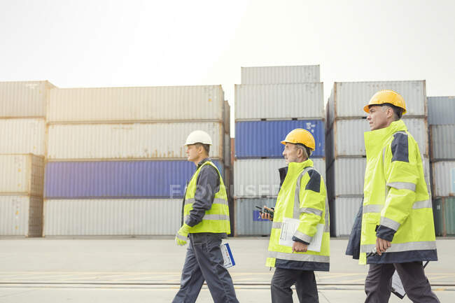 Trabalhadores portuários que caminham ao longo de contentores de carga no estaleiro — Fotografia de Stock