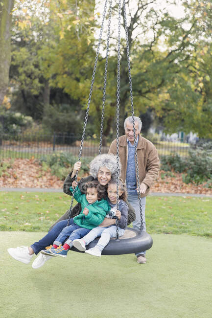 Grandparents and grandchildren playing on tire swing in park — Stock Photo