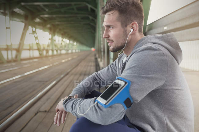Corredor masculino escuchando música con auriculares y smartphone - foto de stock