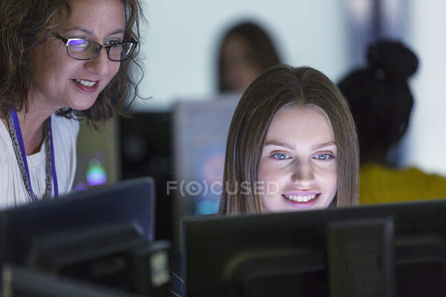 Une enseignante du secondaire aidant un étudiant à l'ordinateur dans un laboratoire informatique — Photo de stock