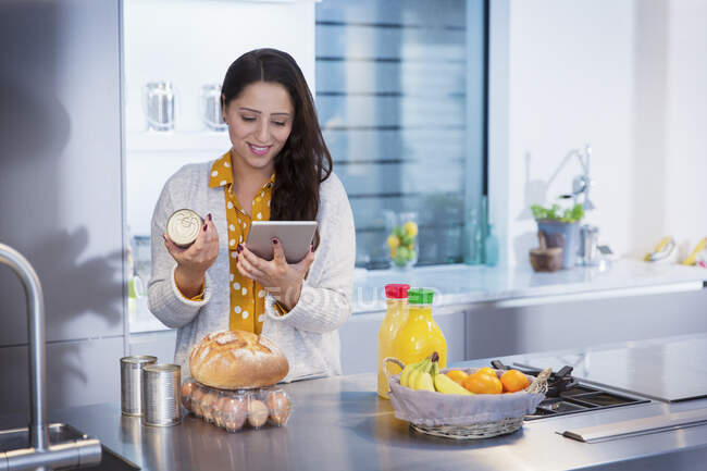 Femme avec tablette numérique vérifiant les étiquettes alimentaires dans la cuisine — Photo de stock