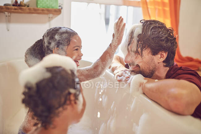 Грайливі дочки в бульбашковій ванні стирають бульбашки на обличчі батьків — стокове фото