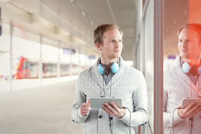 Giovane con tablet digitale e cuffie in attesa vicino alla piattaforma della stazione ferroviaria — Foto stock