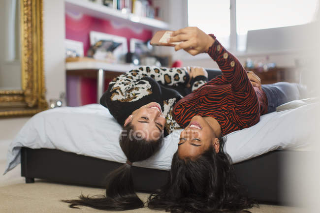 Счастливые девочки-подростки делают селфи вверх ногами на кровати — стоковое фото