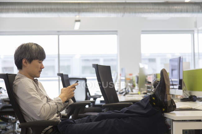 Uomo d'affari che utilizza smart phone con piedi sulla scrivania dell'ufficio — Foto stock