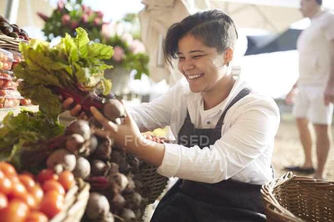 Mujer joven sonriente trabajando, arreglando productos en el mercado de agricultores - foto de stock