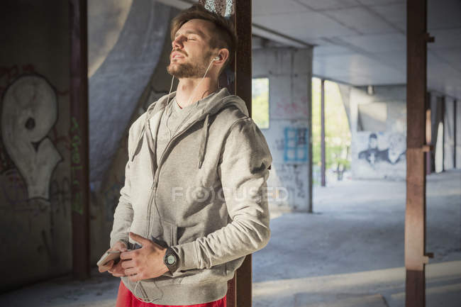 Coureur mâle fatigué écoutant de la musique, se reposant dans un bâtiment abandonné — Photo de stock
