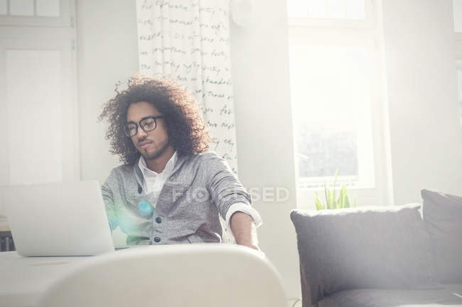Молодой человек работает за ноутбуком в солнечной гостиной — стоковое фото
