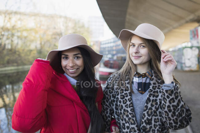 Ritratto fiducioso giovani donne che indossano fedora lungo il canale — Foto stock
