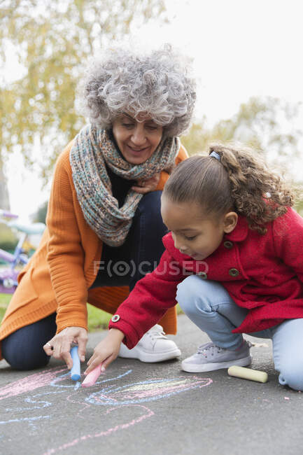 Grandmother and granddaughter drawing with sidewalk chalk — Stock Photo