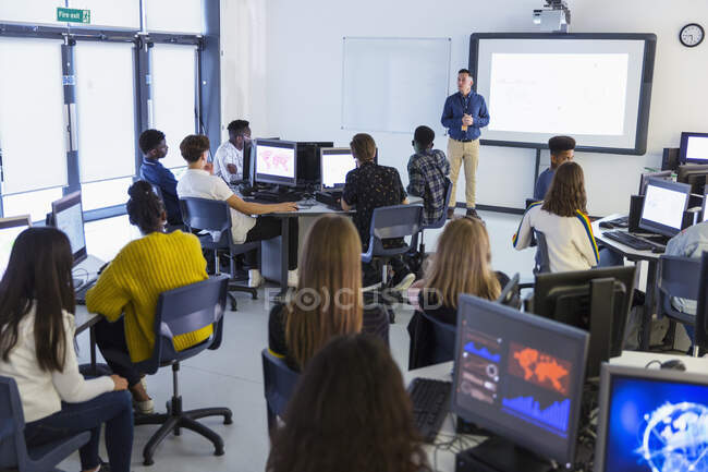 Estudiantes de secundaria en computadoras viendo al profesor en la pantalla de proyección en el aula - foto de stock